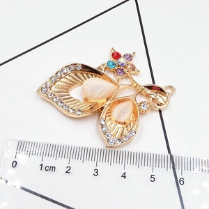Detail view of a vintage gold leaf pendant with rhinestones and measurement scale