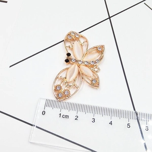 Macro view of golden butterfly accessory with opal stones and rhinestones showing 4cm scale