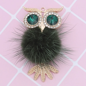 Detailed close-up of a golden owl pendant with dark green fur ball and crystal eyes