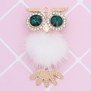 Detail view of owl keychain with white fur ball and green crystal eyes in gold metal