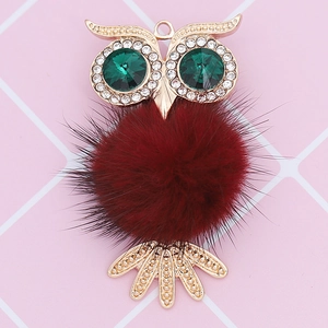 Detail of owl pendant featuring emerald crystal eyes and a plush burgundy fur body