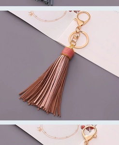 Detail of rose gold faux leather tassel keychain with red stitching and gold lobster clasp