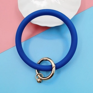 Blue silicone wristlet keychain with a gold metal ring on a pastel two-tone background