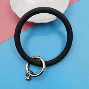 Detail of matte black silicone wristlet keychain with gold spring ring on pastel background