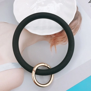 Minimalist black silicone wristband keychain with gold metal clasp on a white tray