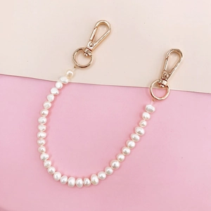 Detail of DIY pearl phone chain featuring white pearls and polished gold lobster clasps