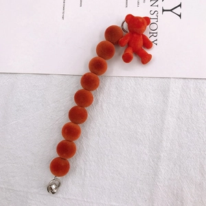 Dettaglio di un ciondolo a forma di orso rosso floccato e cinturino di perle su tessuto