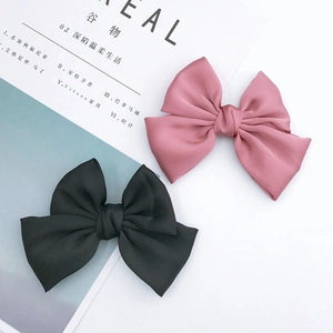 Detail of oversized satin bow hair clips in pastel pink and black on a magazine