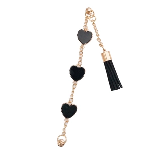 Bracelet chaîne dorée élégant avec breloques cœurs noirs et pendentif pompon sur fond blanc