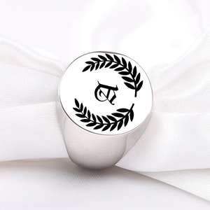 Close-up of silver signet ring with engraved Gothic letter C and laurel leaves on white silk