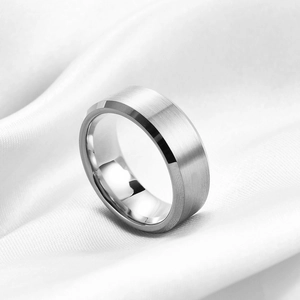 Macro detail of brushed silver tungsten ring with beveled edges on white silk fabric