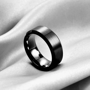 Macro shot of brushed black stainless steel ring with beveled edges on silk