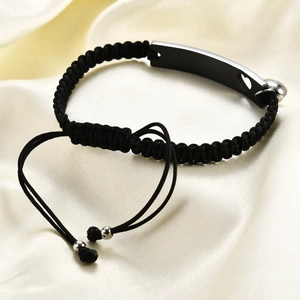 Macro shot of black woven couple bracelet featuring a heart cutout and metal plate
