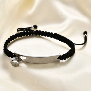 Detailed macro of black braided couple bracelet with silver heart cutout metal plate