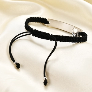 Macro detail of hand-woven black cord bracelet featuring a polished heart cutout metal plate