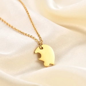 Macro view of polished gold stainless steel heart puzzle necklace on silk fabric