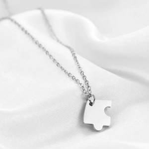 Macro shot of polished stainless steel puzzle piece pendant on white silk fabric
