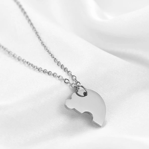 Macro shot of polished stainless steel heart puzzle necklace on white silk fabric background