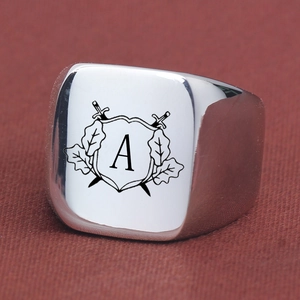 Polished silver signet ring with engraved heraldic shield and swords on red fabric