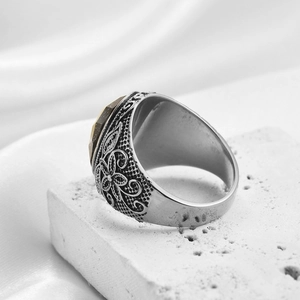 Dettaglio macro di anello retrò in acciaio con rilievi floreali e gemma marrone sfaccettata
