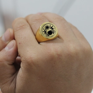 Detailaufnahme eines goldenen Siegelrings aus Edelstahl mit Krebs- und Sonnengravur am Finger