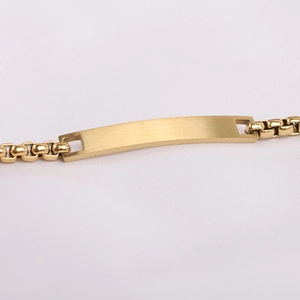 Detailed macro view of a gold-plated box chain bracelet with a brushed metal nameplate