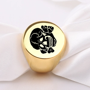 Macro shot of gold stainless steel signet ring with black skull design on white satin