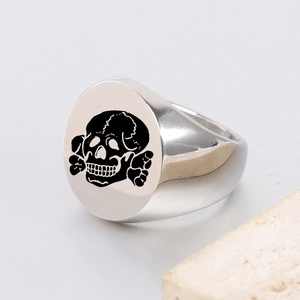 Macro detail of polished stainless steel signet ring featuring a black skull engraving