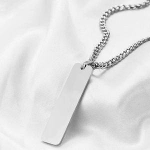 Close-up of polished stainless steel rectangular bar pendant on a silk fabric background