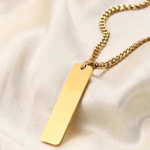 Polished gold stainless steel bar pendant necklace with Cuban chain on silk fabric