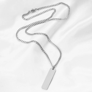 Macro shot of polished silver rectangle pendant with fine curb chain on white silk background