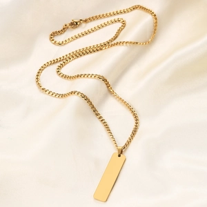 Detailed view of 40mm golden vertical bar pendant on Cuban chain over silk fabric