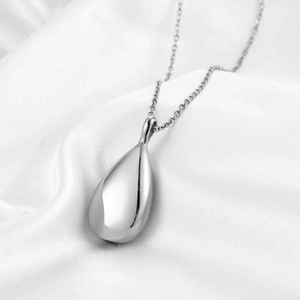 Close-up of polished silver teardrop cremation urn necklace on elegant white silk background