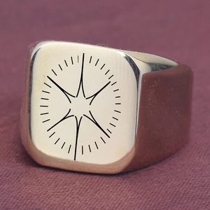 Détail d'une bague chevalière carrée dorée avec motif étoile gravé sur tissu