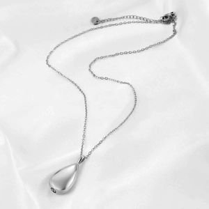 Macro view of silver teardrop memorial urn necklace with screw bottom on silk background
