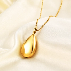 Close-up of golden teardrop urn necklace on silk background with polished mirror finish