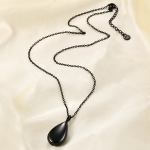 Detail of black teardrop urn necklace for ashes on beige silk background
