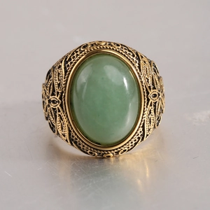 Gros plan d'une bague dorée vintage avec pierre verte ovale et motifs gravés