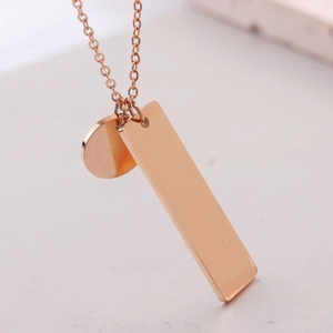 Primer plano de un colgante rectangular y circular de oro rosa con cadena de acero pulido