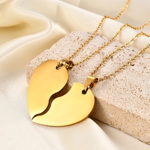 Close-up of golden puzzle heart necklaces on beige silk fabric and stone base