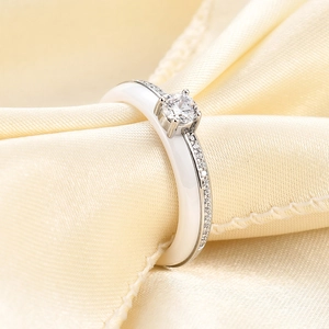 Close-up of white ceramic ring with round zircon inlay on elegant champagne silk fabric