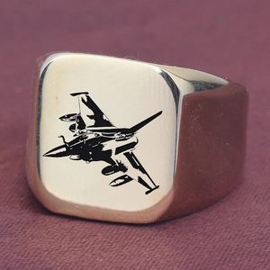 Makroaufnahme eines goldenen Siegelrings mit Lasergravur eines Kampfflugzeugs auf quadratischem Feld