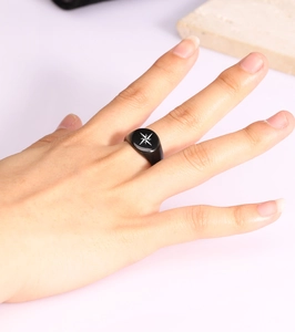 Close-up of a 12mm black polished signet ring with an engraved North Star pattern on index finger