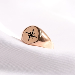 Close-up of rose gold signet ring with black octagram star on white silk texture