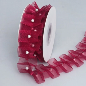 Close-up of wine red ruffled mesh lace trim with white pearls on a spool