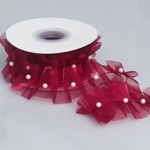 Close-up of wine red ruffled mesh ribbon with white pearls wound on a white spool