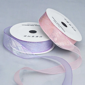 Detail von lavendel und rosa Organzabändern mit silberner Wellenprägung auf weißen Spulen