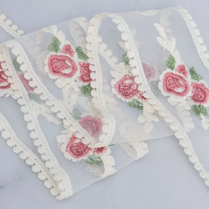 Detail of floral embroidery on ivory mesh lace ribbon with pink roses and green leaves