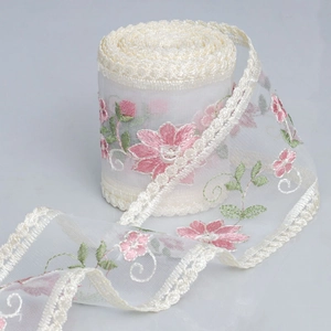 Detail of embroidered floral lace ribbon with pink flowers on off-white mesh net
