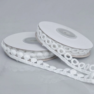 Close-up of white water-soluble lace rolls with ball fringe and geometric embroidery details